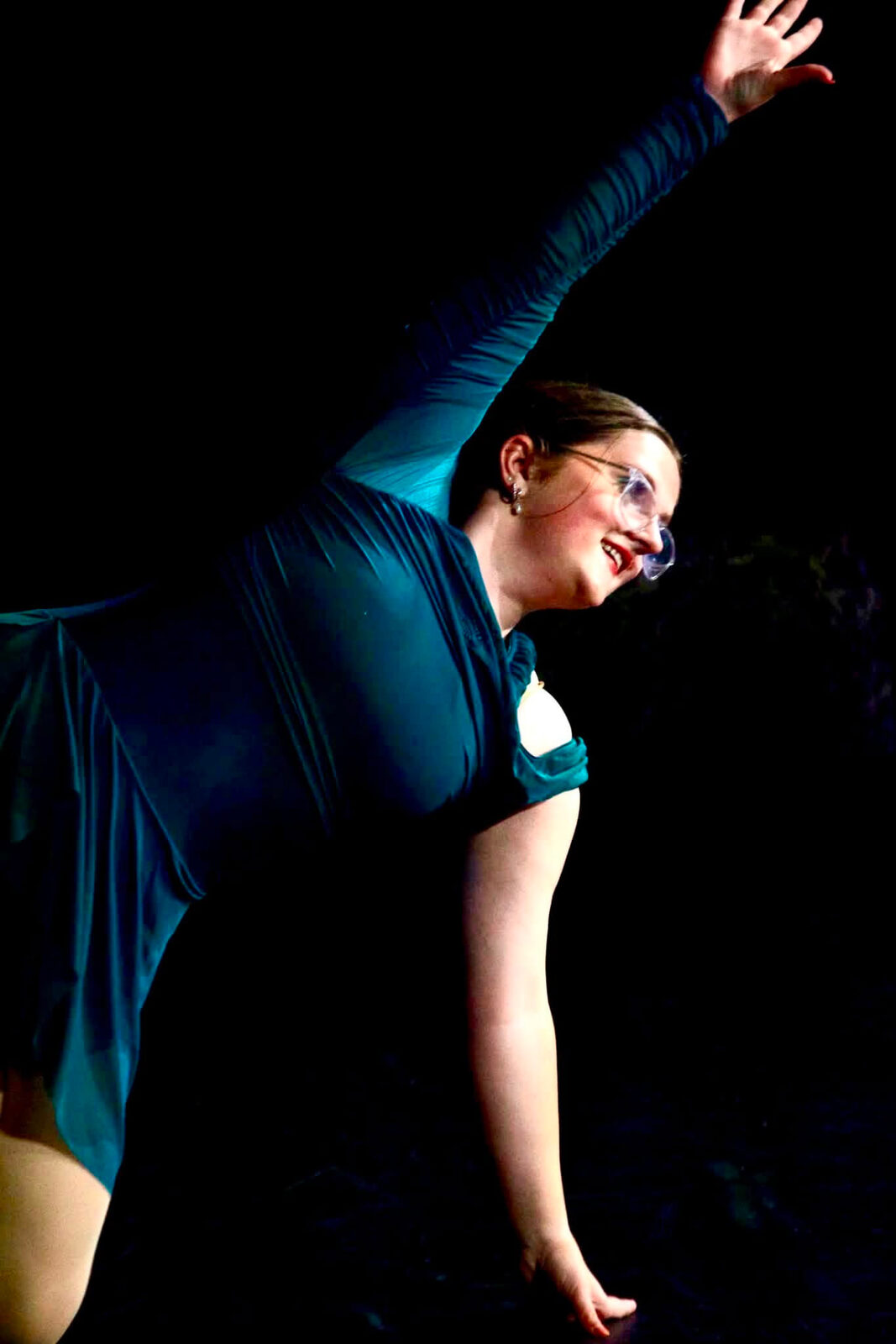 A dancer in teal reaching upward during a stage performance