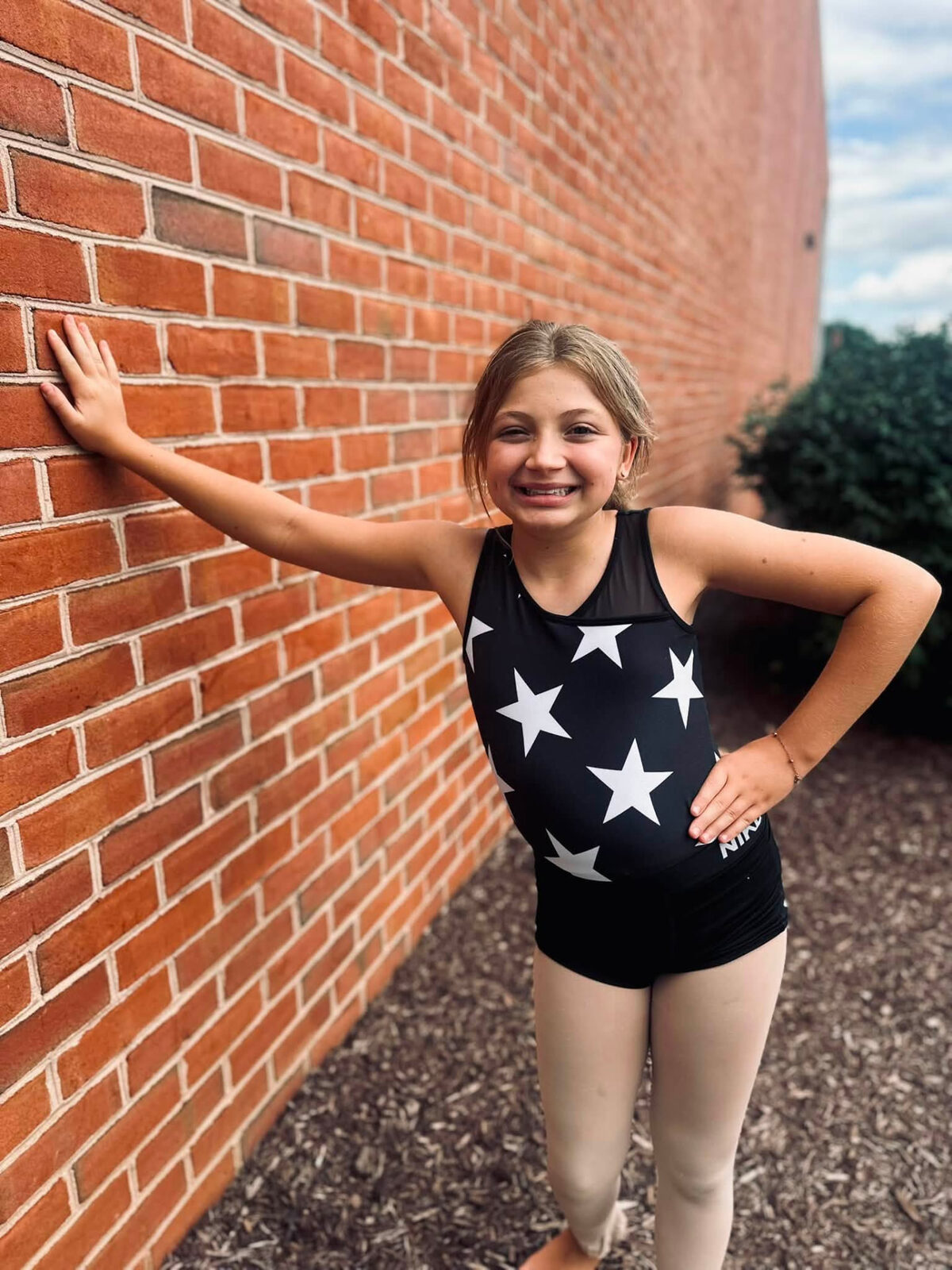 A young dancer smiling beside a brick wall